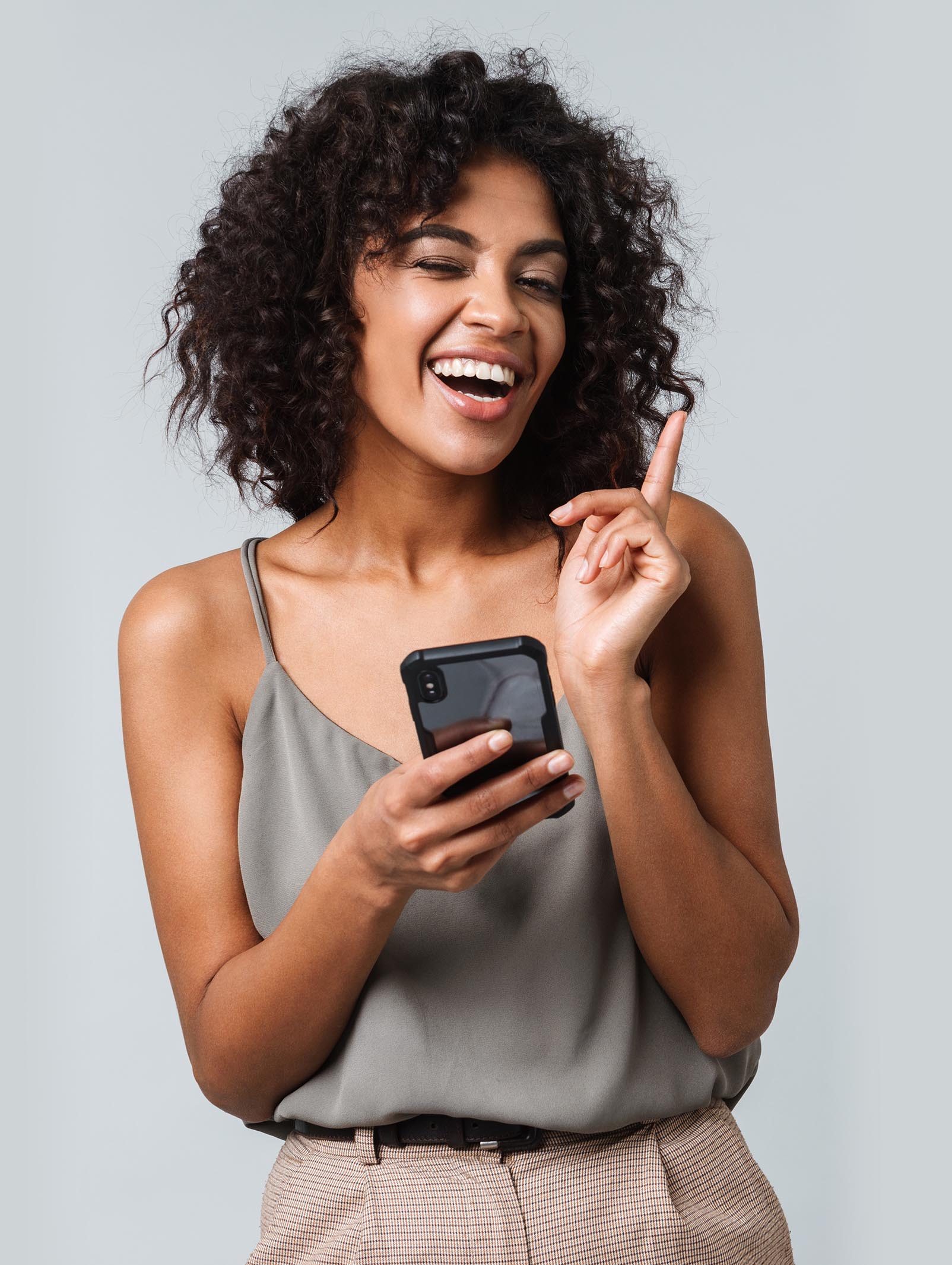 Happy young african woman casually dressed standing isolated over gray background, using mobile phone